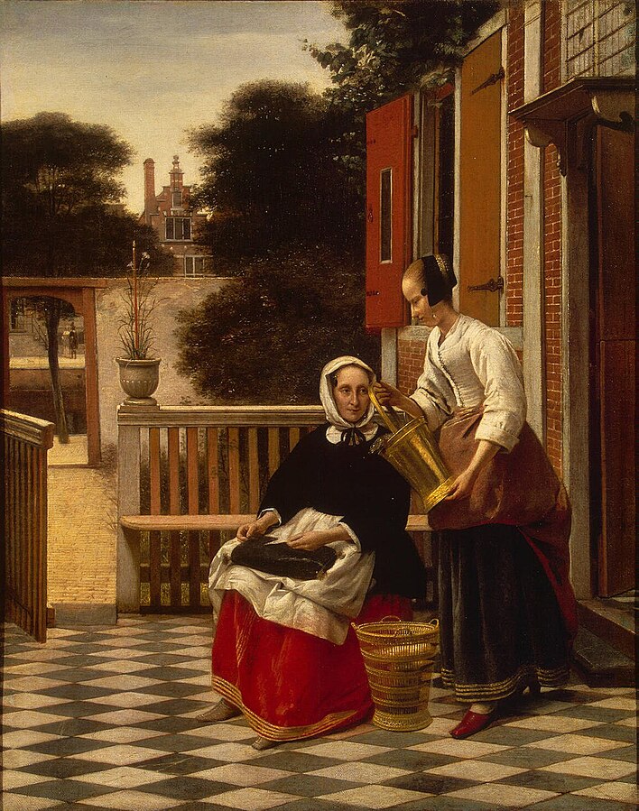 An older woman sits on a black and white tiled patio outside a house. A younger maid stands next to her holding a pail