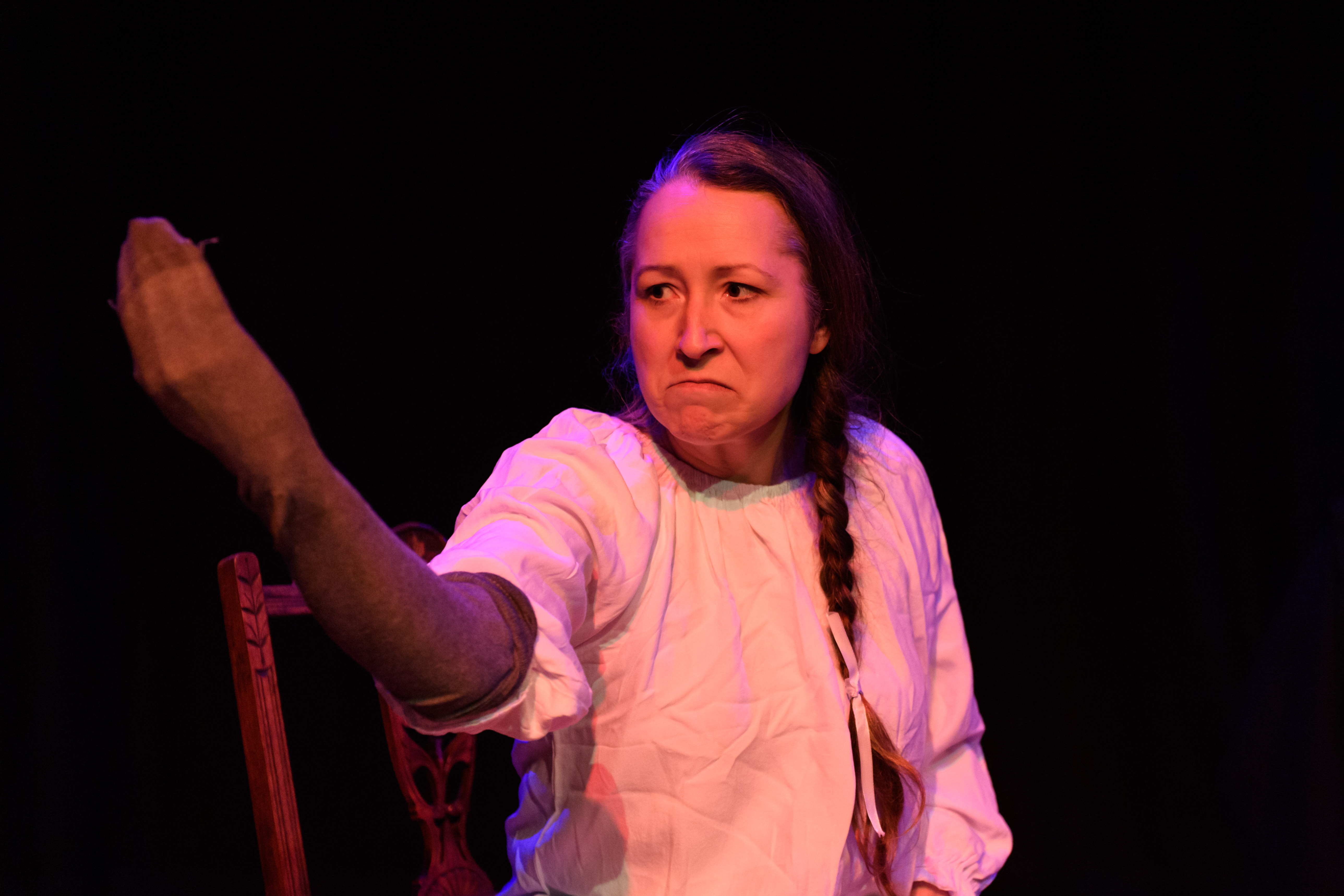 A photograph of a white actress in a white gown sits on a chair staring menacingly at a stocking puppet on her own hand
