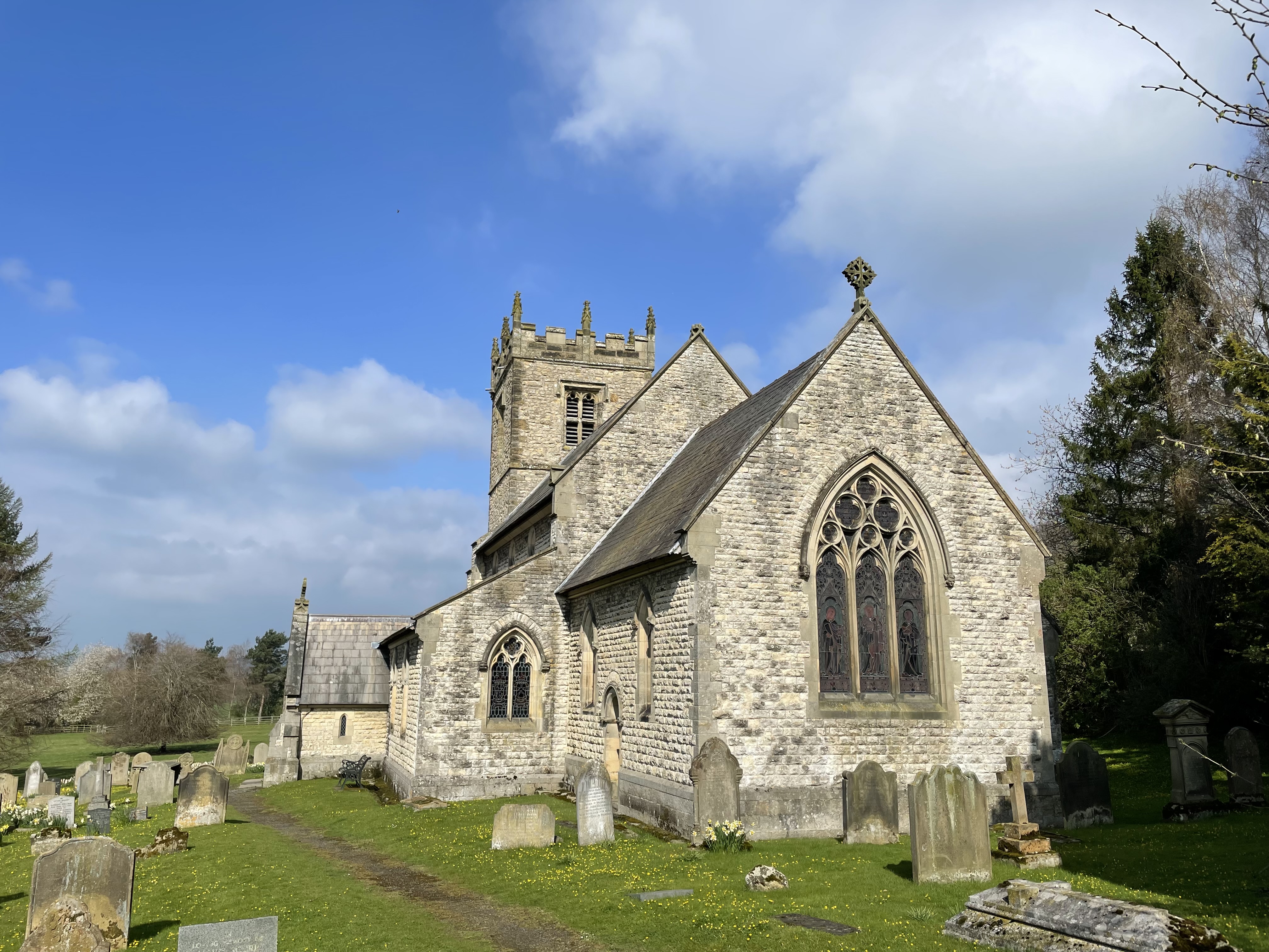 The view of the back end of a stone church, in a graveyard, in summer.